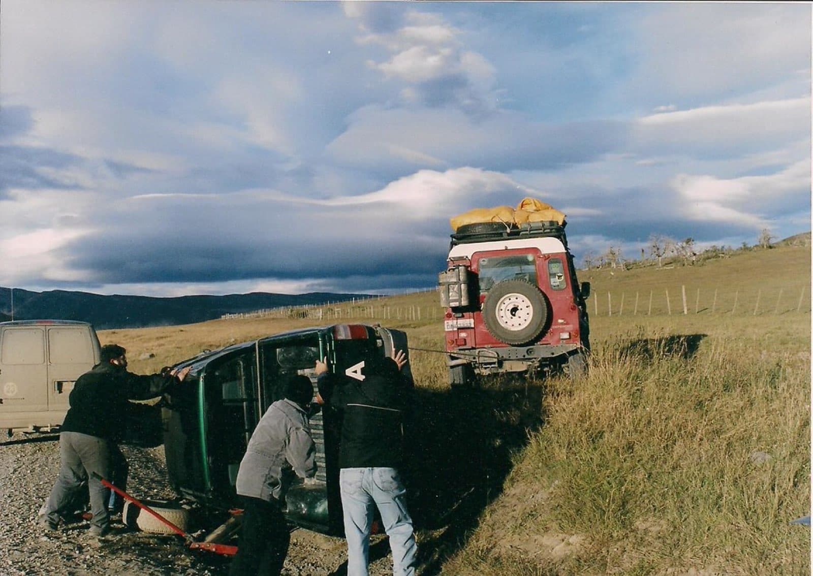 Travellers working together to right a tipped Defender on a gravel road in Patagonia
